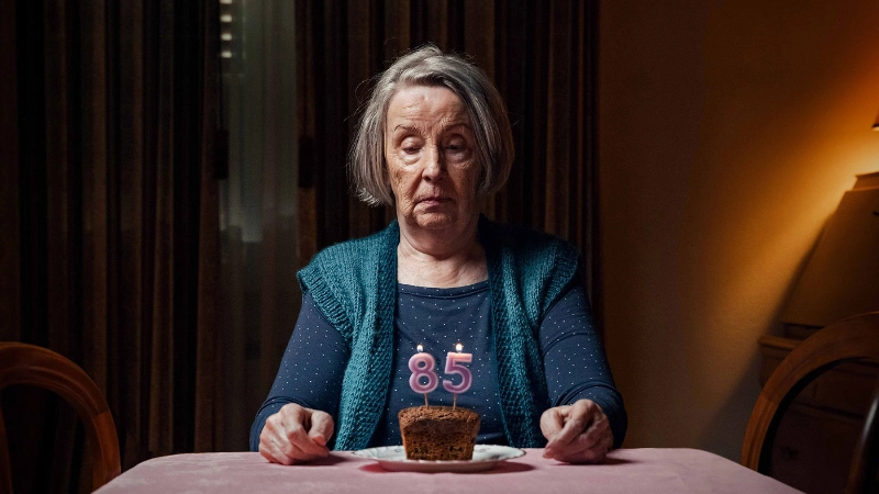 Una donna sola si siede a un tavolo e guarda con tristezza la sua torta di compleanno