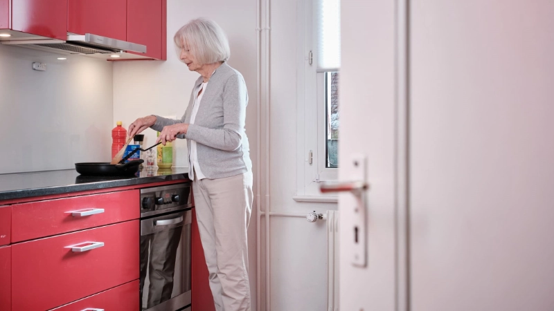 Signora anziana che cucina ai fornelli in cucina.