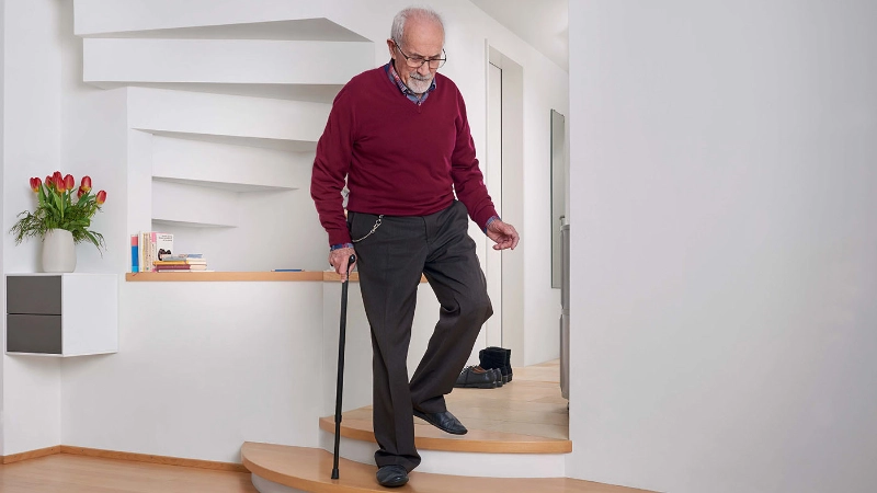 Un homme âgé descend prudemment les escaliers en s'aidant d'une canne.