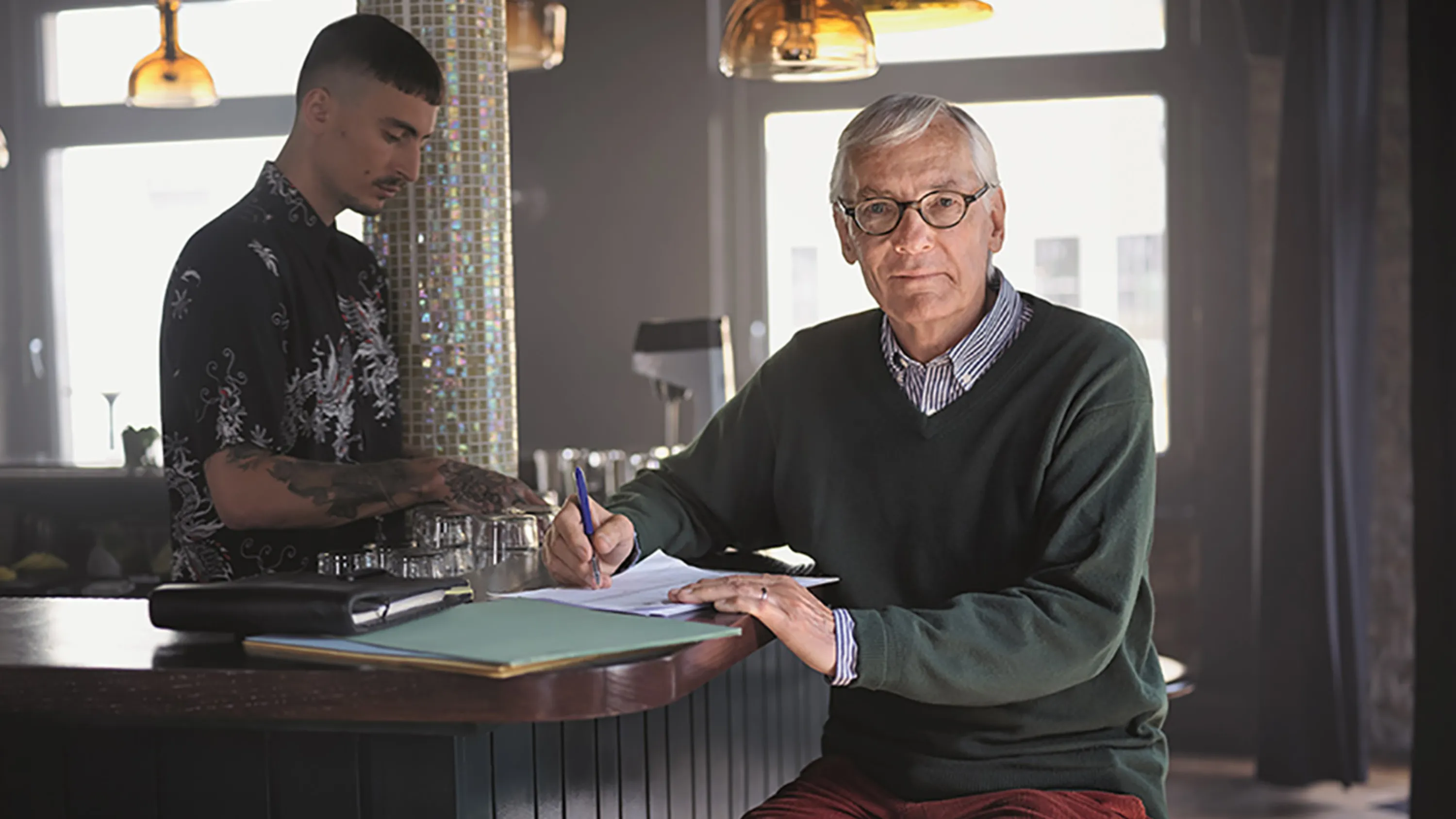 Un homme âgé est assis au bar d'un café et vérifie des documents.