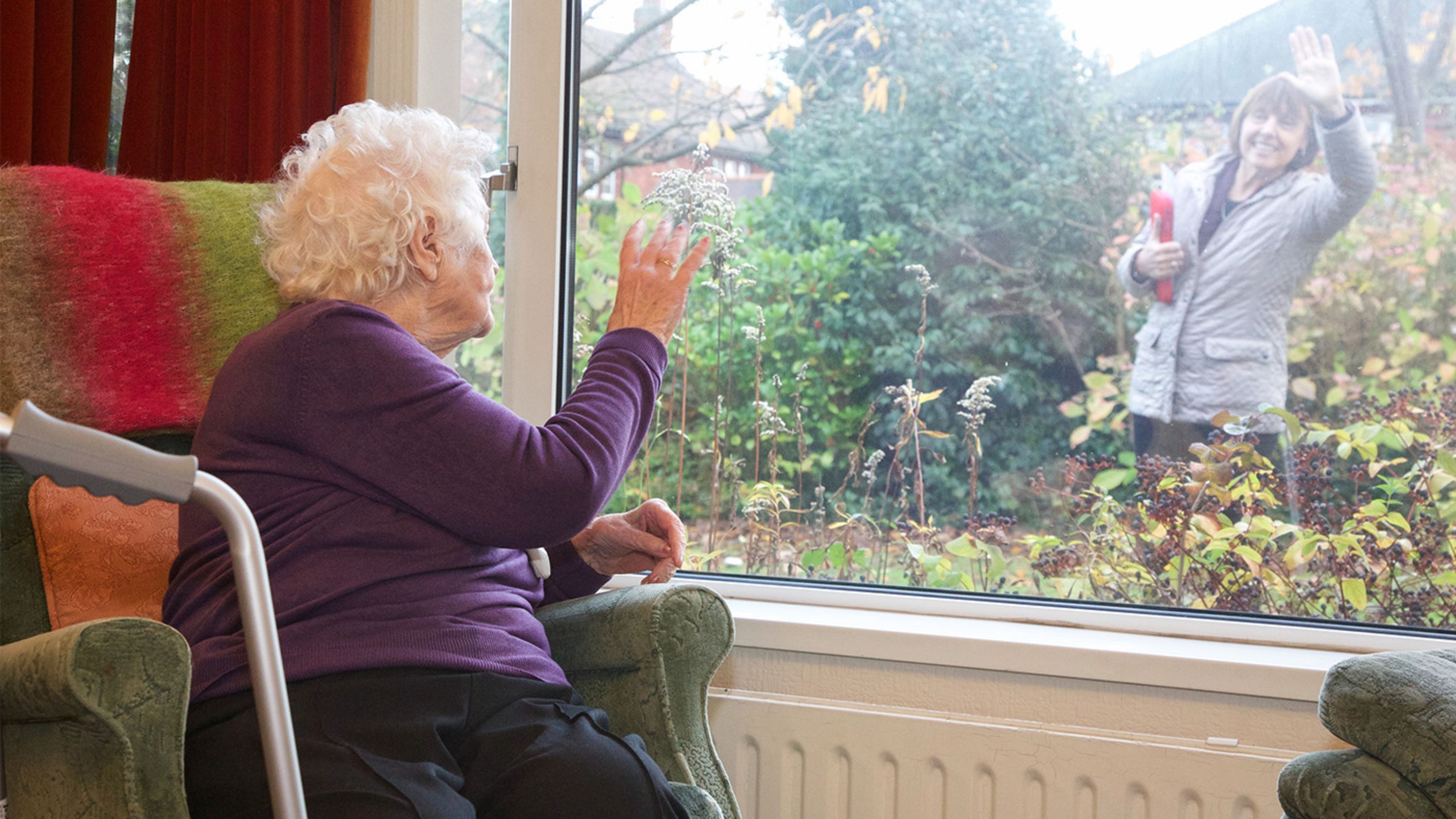 Ältere Dame sitzt am Fenster und winkt der Nachbarin