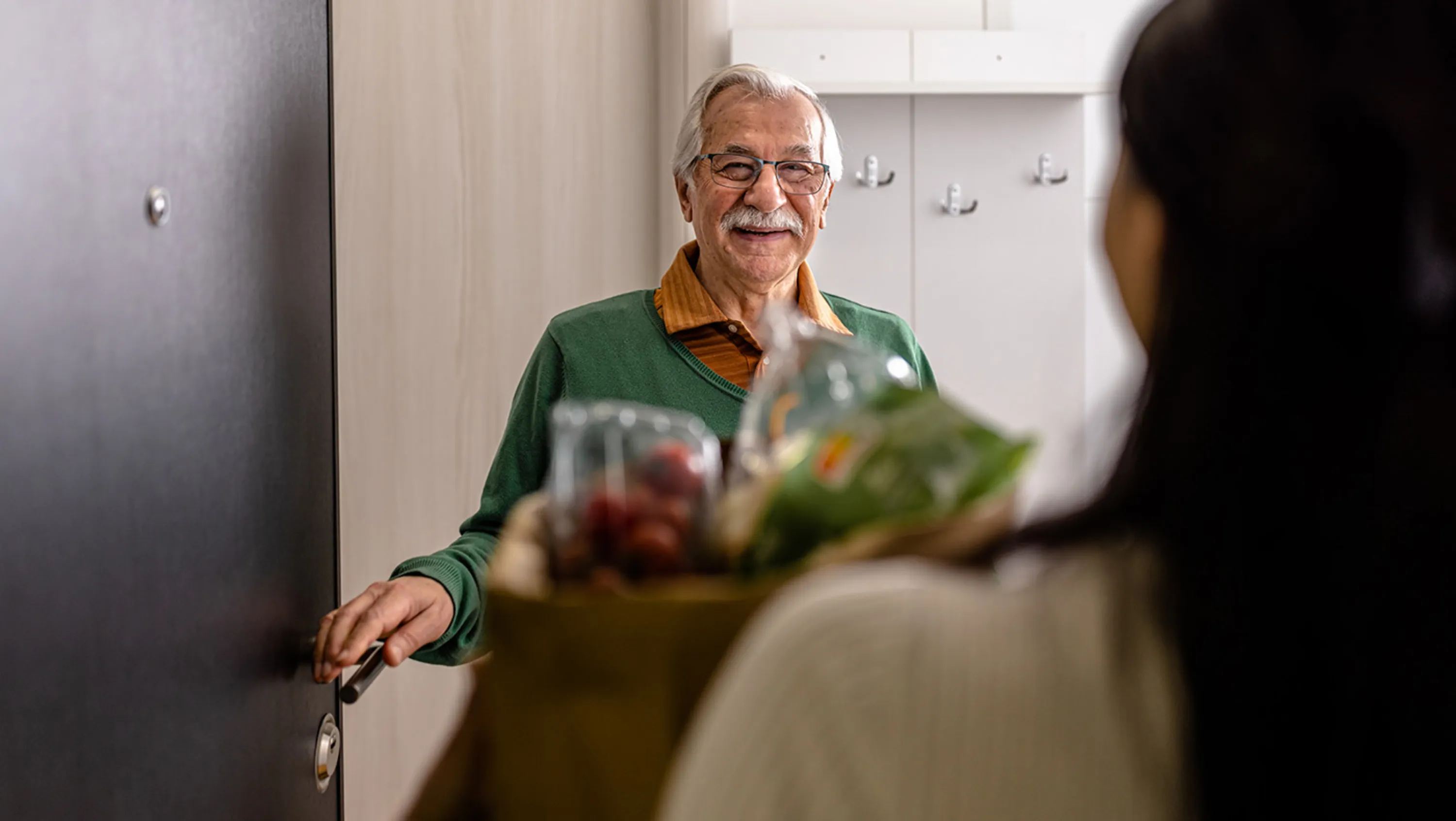 Frau übergibt älterer Frau eine Tasche mit Lebensmittel