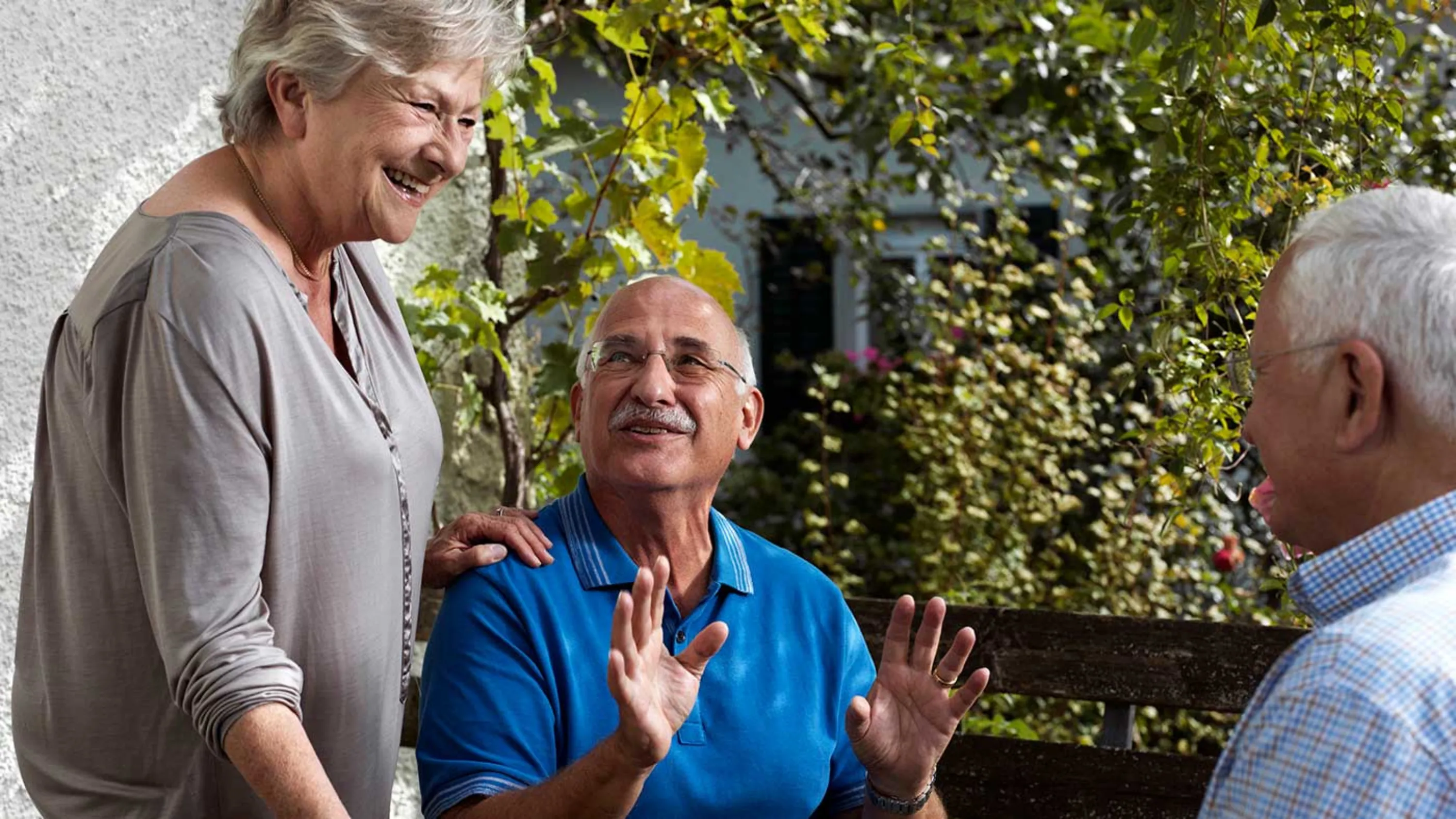 Drei Seniorinnen und Senioren im Gespräch auf einem Balkon.