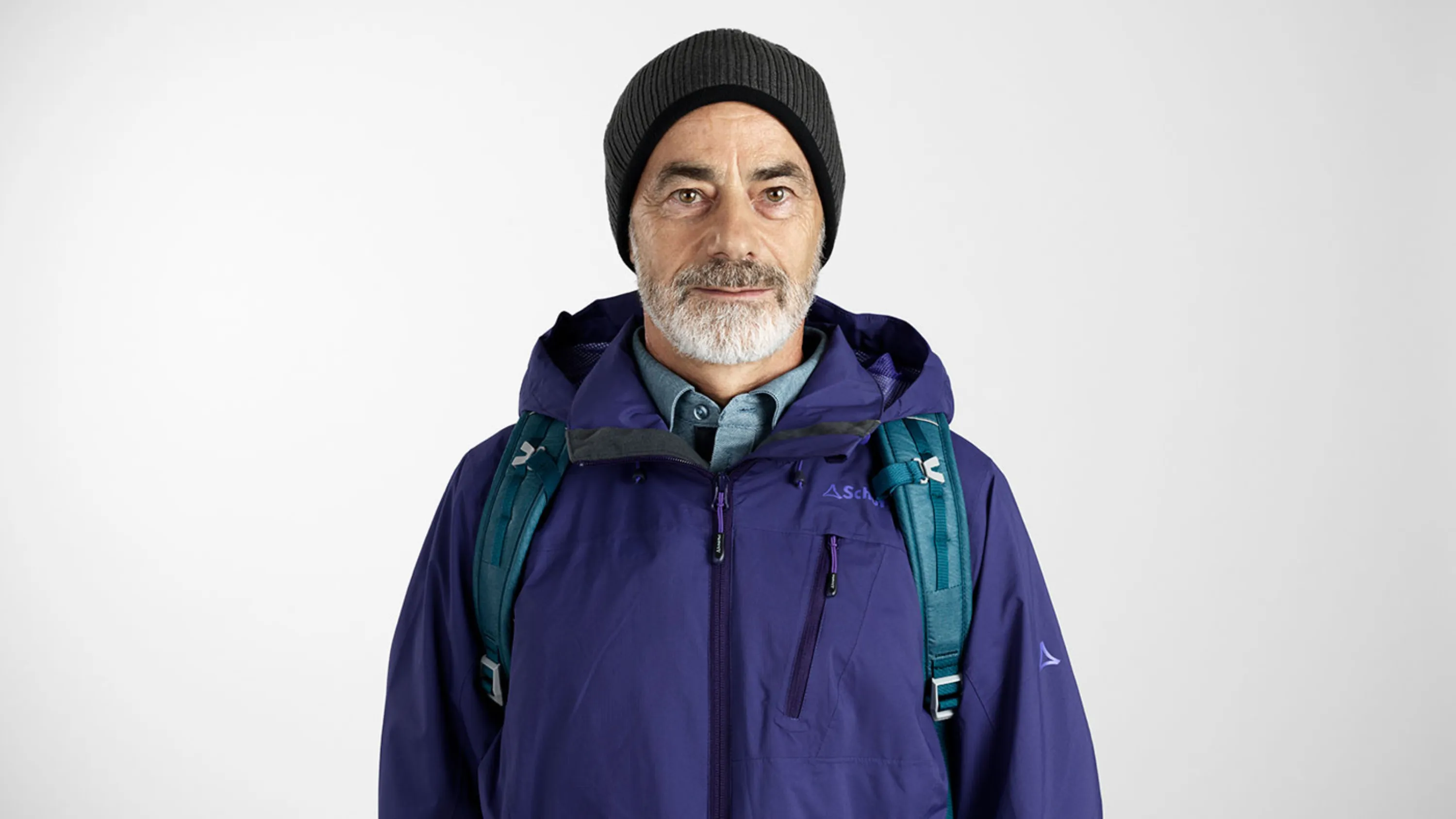 Portait eines älteren Herrn in Regenjacke und Mütze sowie Rucksack.