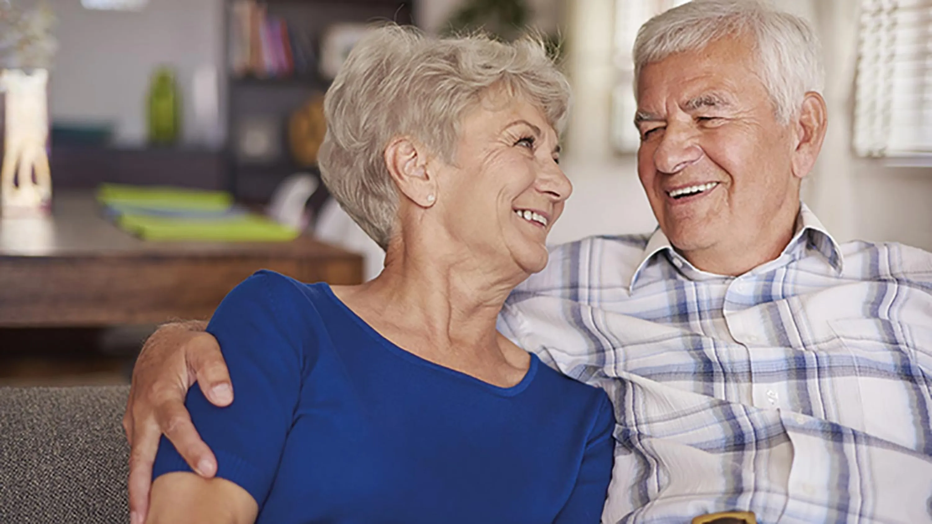 Ein pensioniertes Paar sitzt Arm in Arm auf einer Bank.