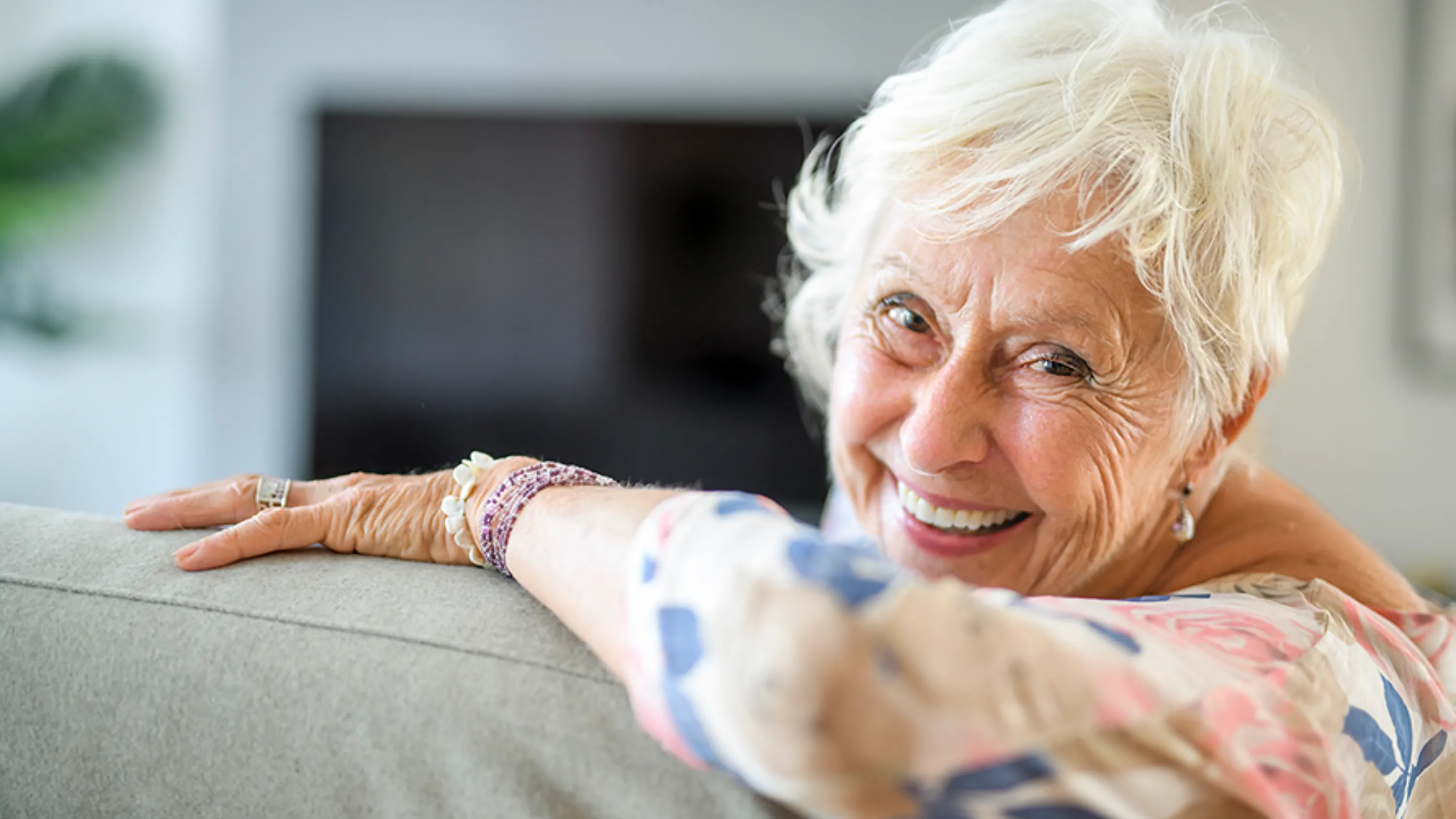 ältere Frau auf Sofa lachend in Kamera