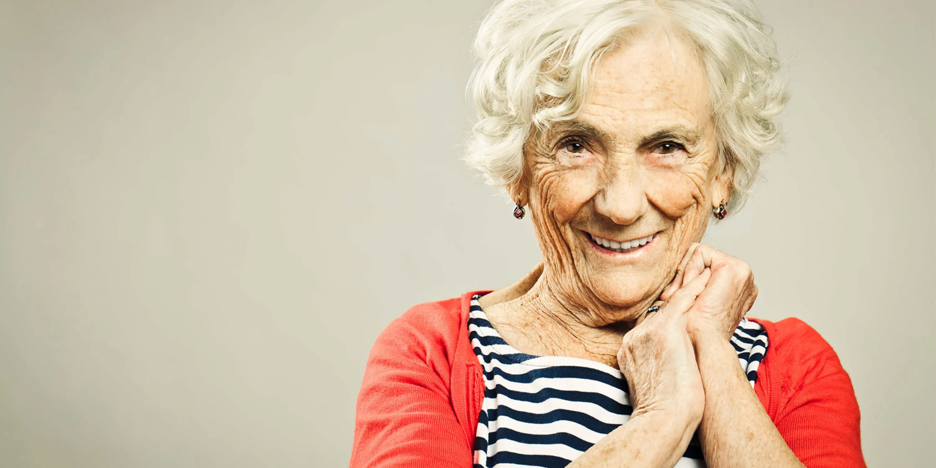 ältere Frau mit blauem Strickpullover und halblangen grauen Haaren schaut in die Kamera