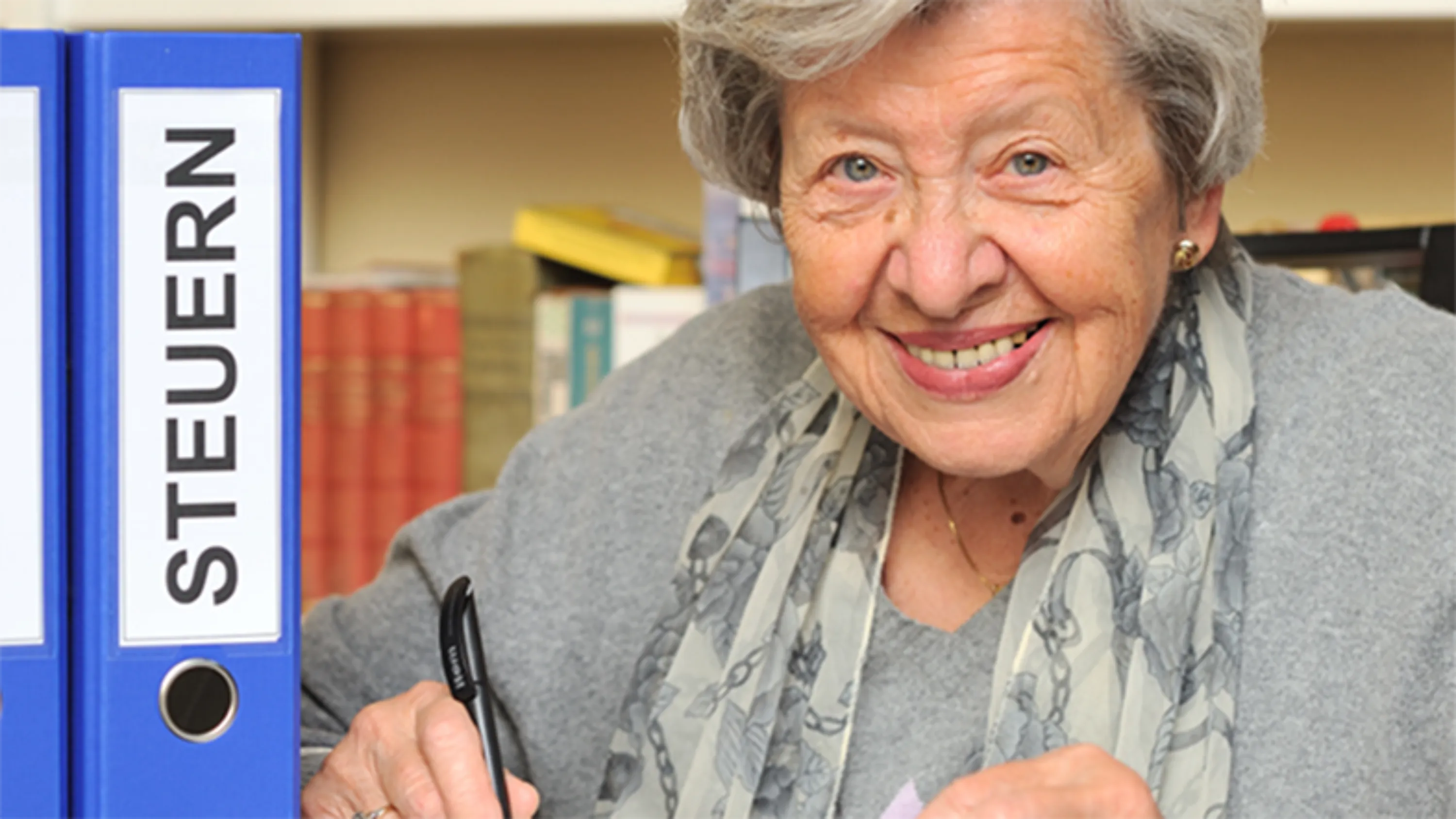 Frau schaut in Kamera mit Ordner Steuern daneben