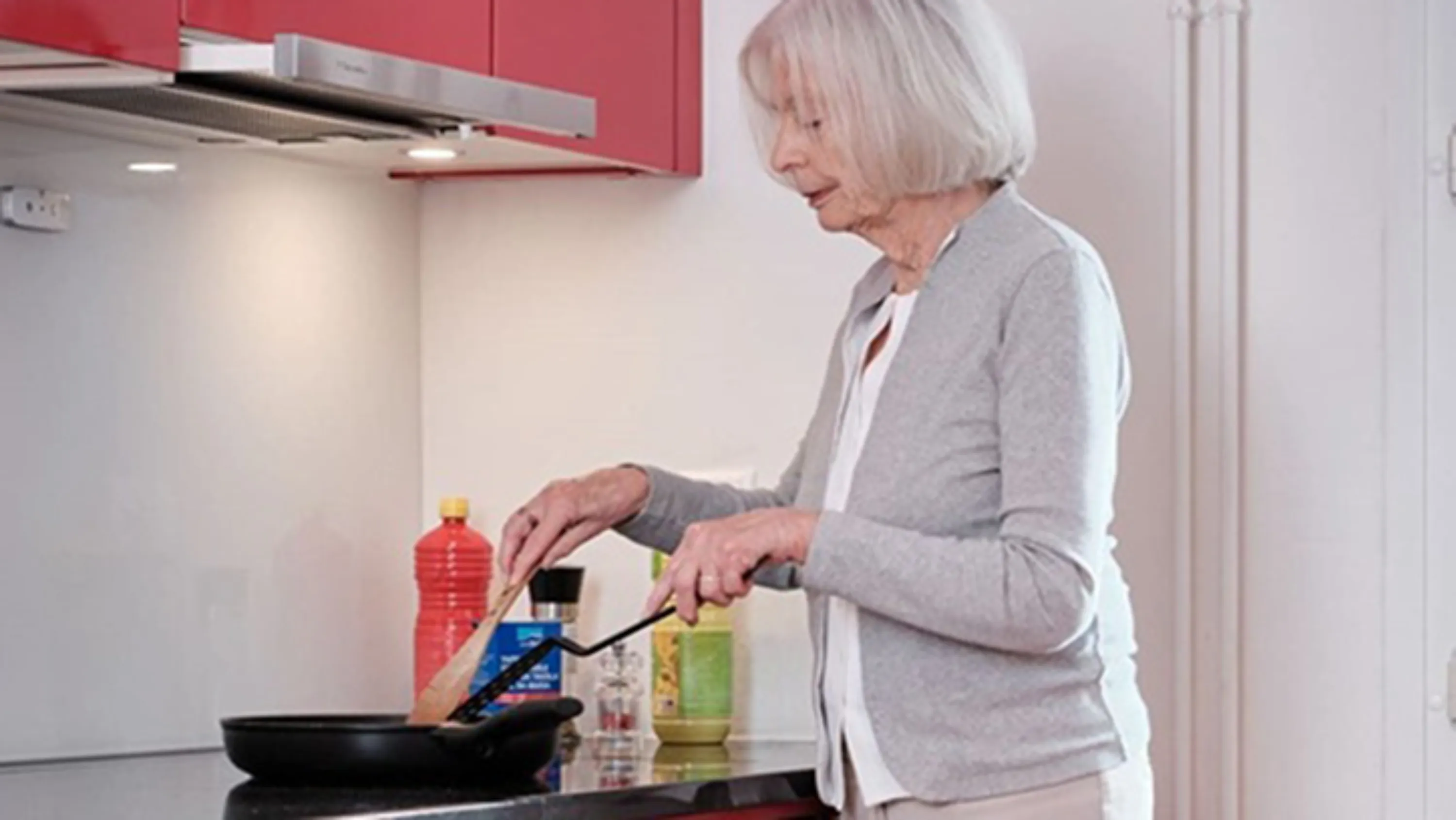 Frau am Herd mit Pfanne am Kochen