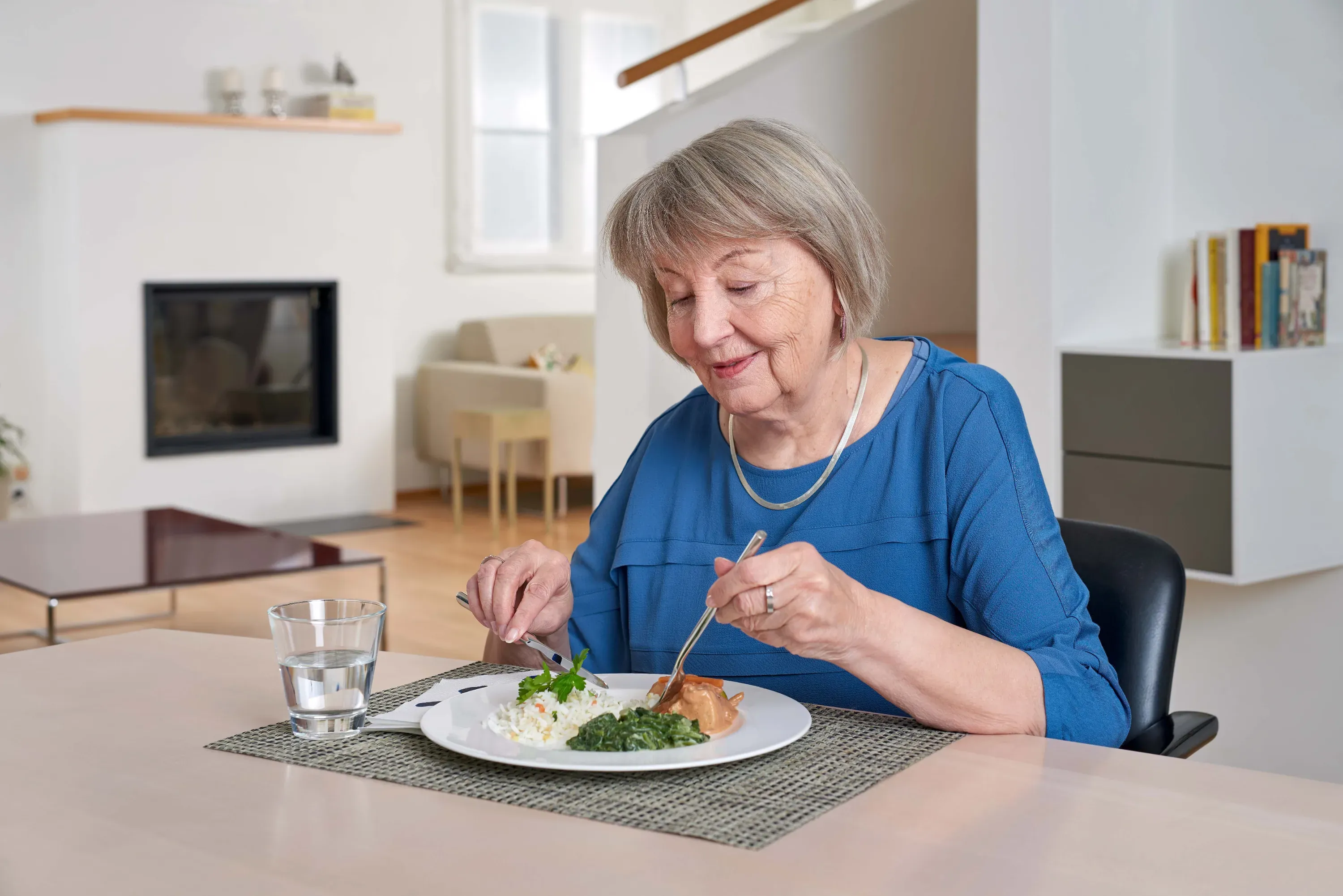 Sympathische Seniorin beim Mittagessen zu Hause
