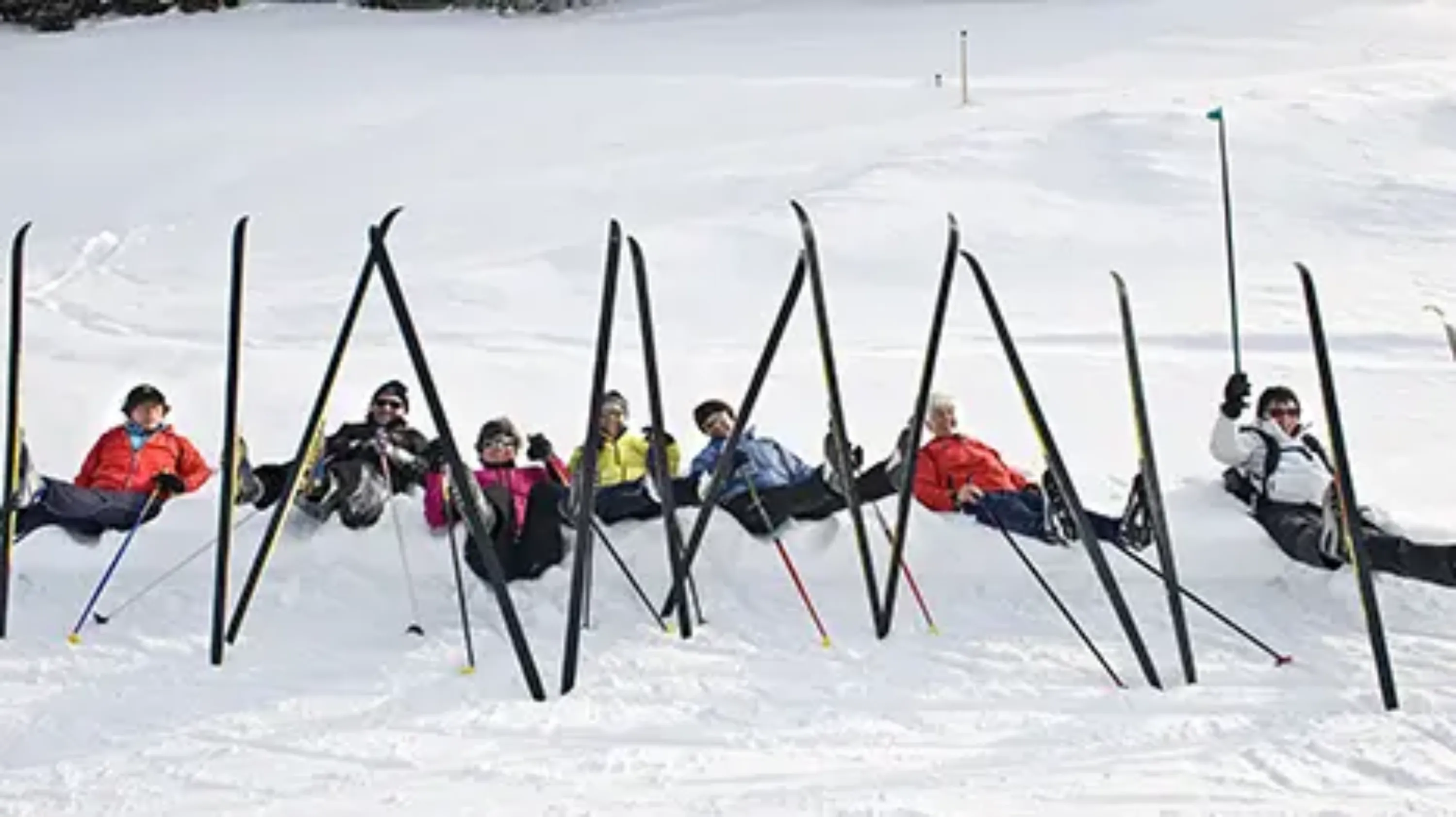groupe de personnes allongées dans la neige, avec les skis de fonds en l'air 