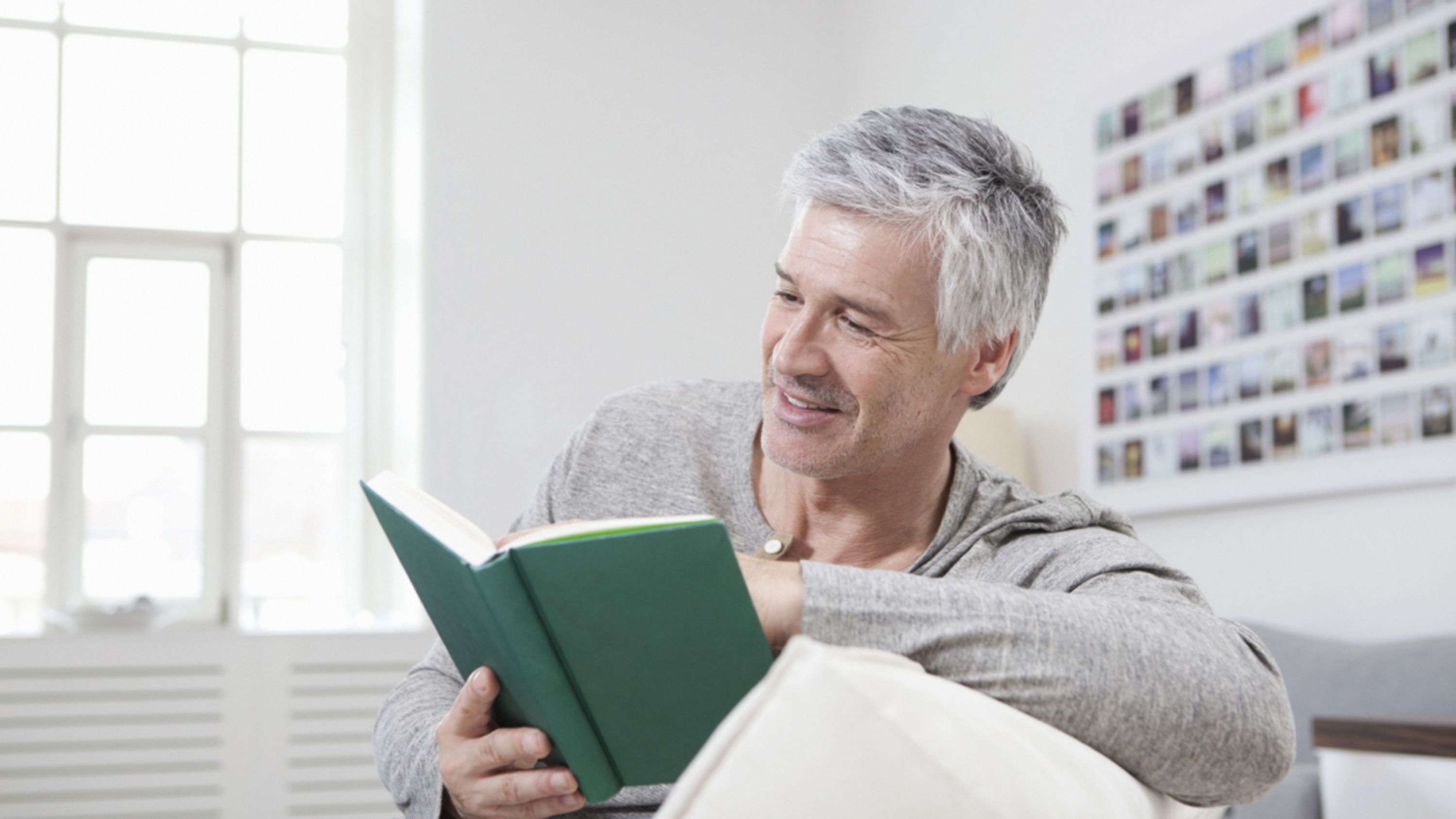 Ein Senior sitzt gemütlich auf dem Sofa und liest ein Buch