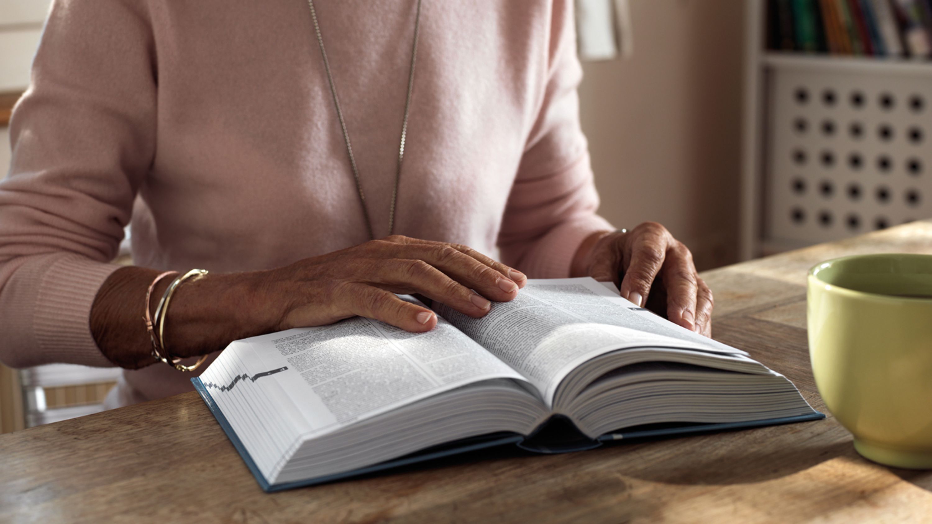Verwitwete Seniorin blättert durch ein Buch in ihrem Wohnzimmer. 