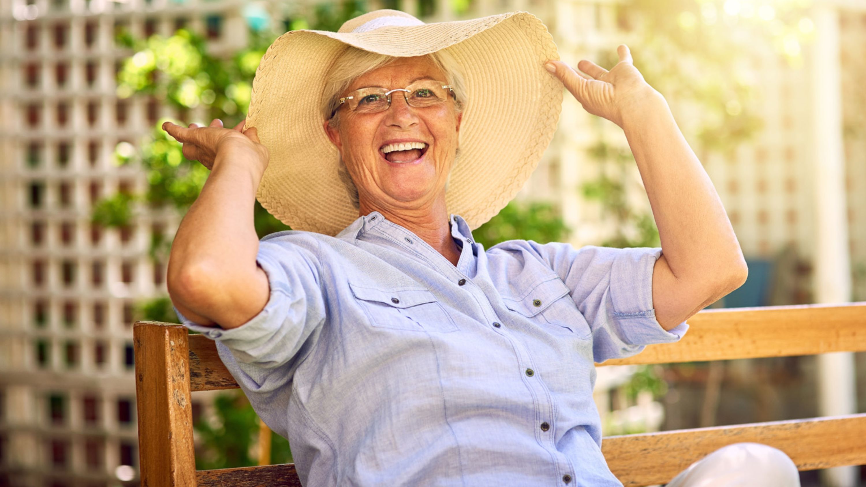 Une dame âgée avec un chapeau est assise sur un banc en été.