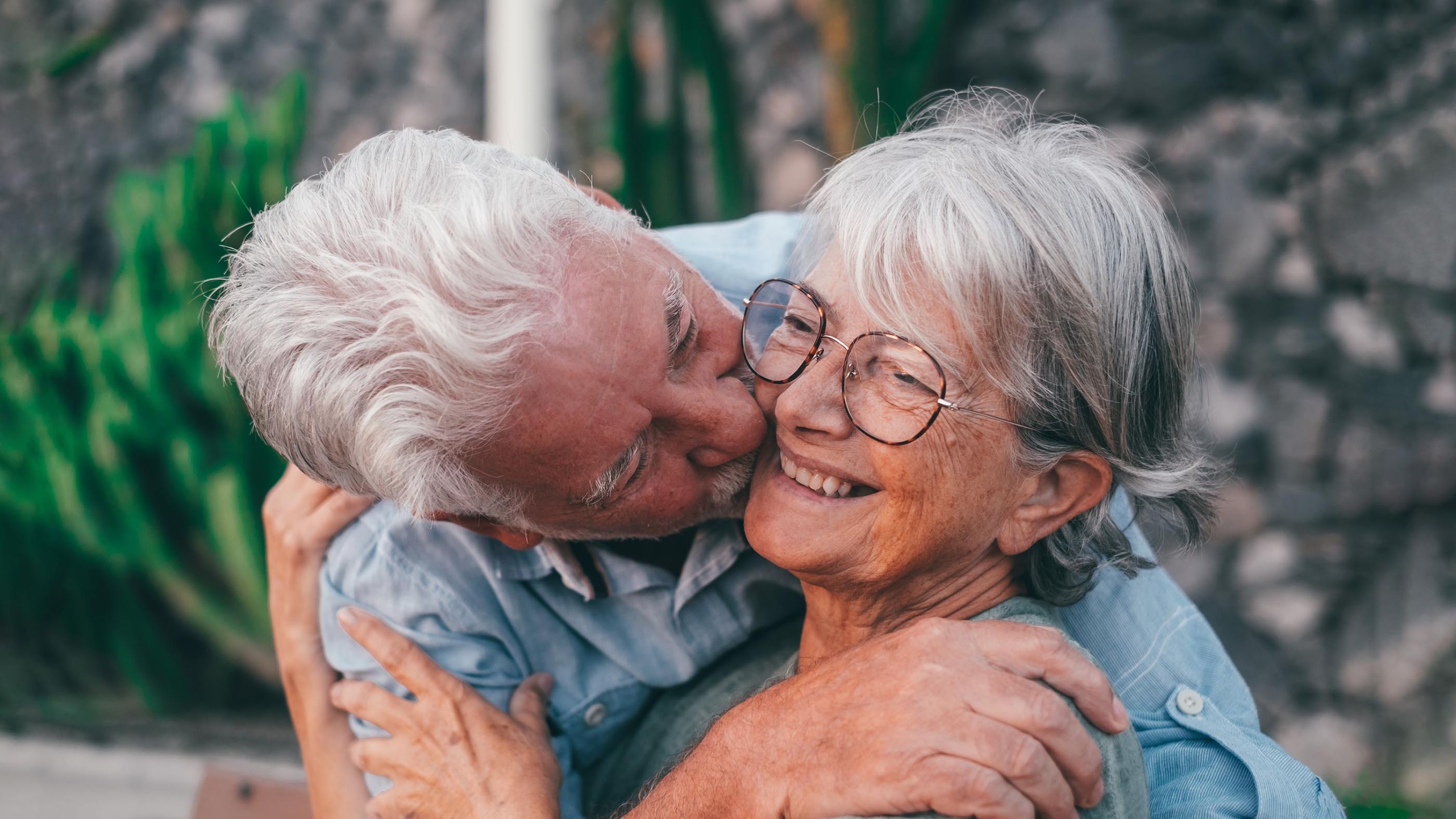 Älterer Mann umarmt eine ältere Frau und küsst sie auf die Wange.