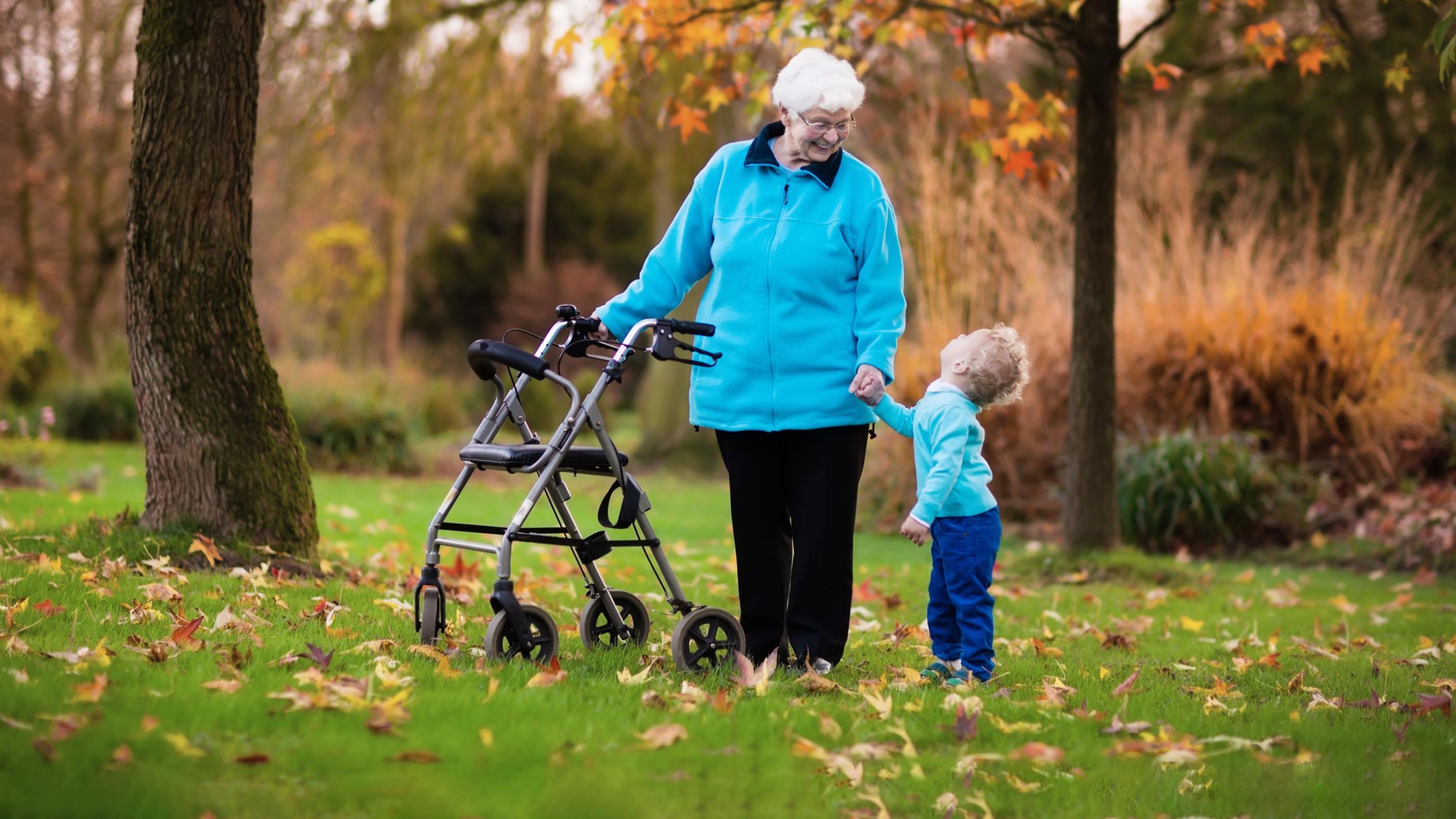 Dans un jardin d'automne, la grand-mère en déambulateur tient la main de son petit-fils et lui sourit.