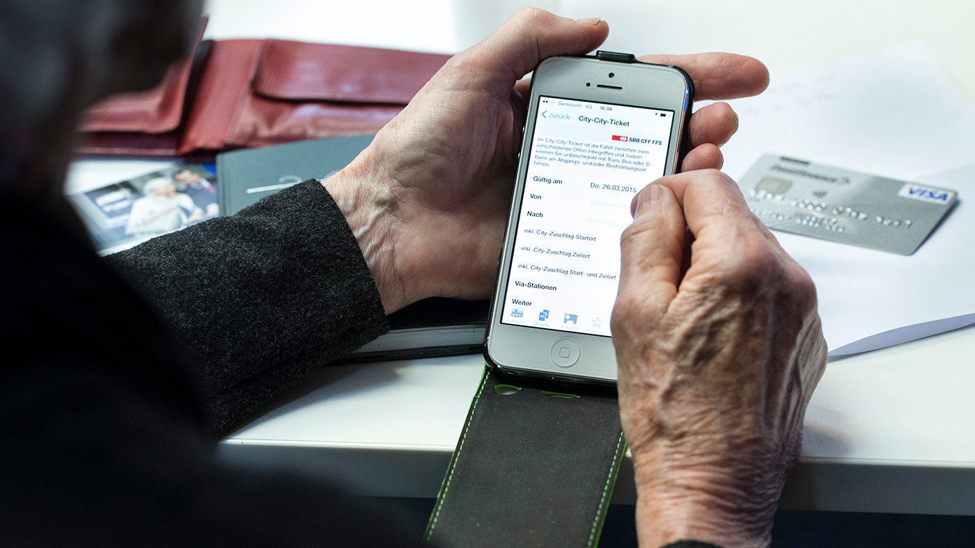 Un anziano tiene in mano uno smartphone con un'app delle FFS.