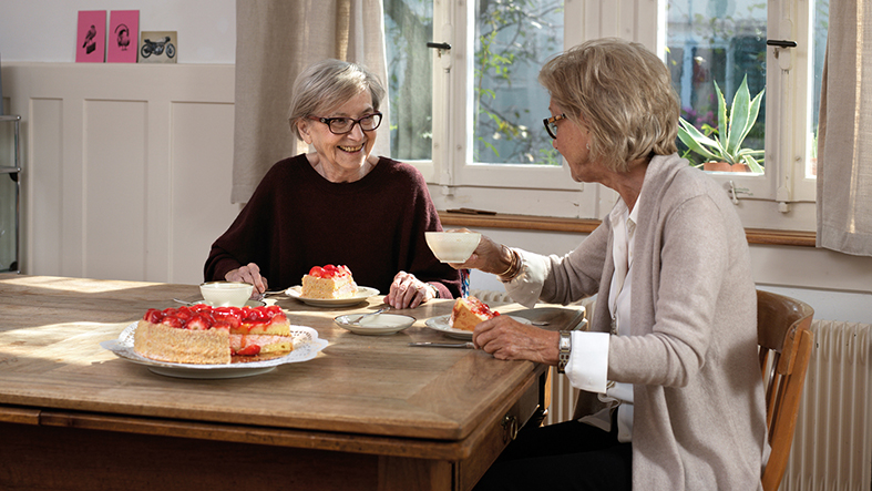 Une bénévole est assise à la table d'une personne âgée.