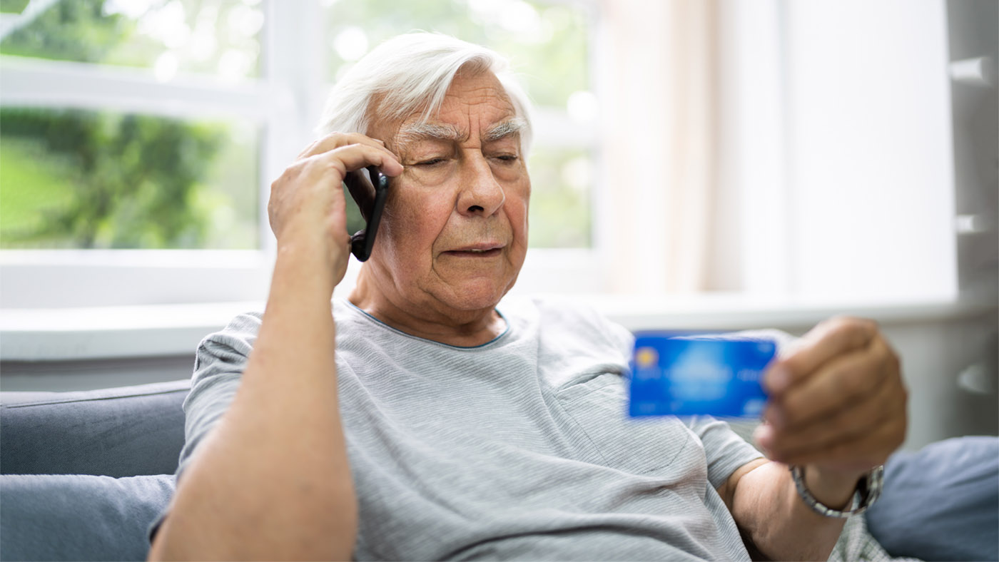 Ein älterer Herr ist am Telefon und schaut auf seine Kreditkarte.