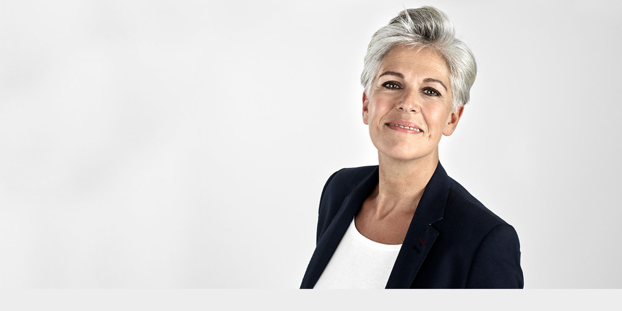 Eine Frau mit grau melierten Haaren und Blazer blickt freundlich in die Kamera.