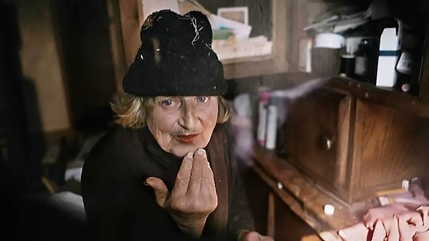 Une femme âgée portant un bonnet noir se touche le menton avec la main.