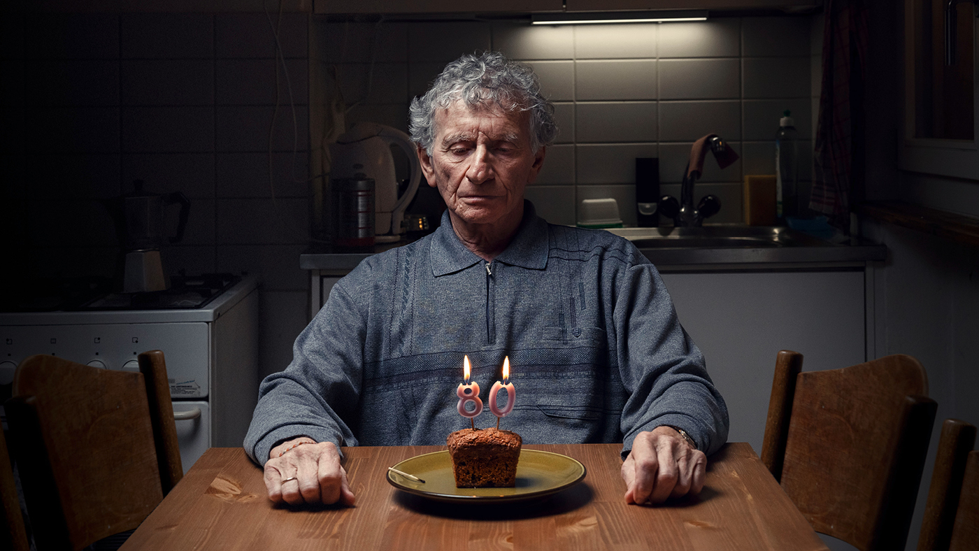 Eine Seniorin sitzt alleine vor einem kleinen Geburtstagskuchen.