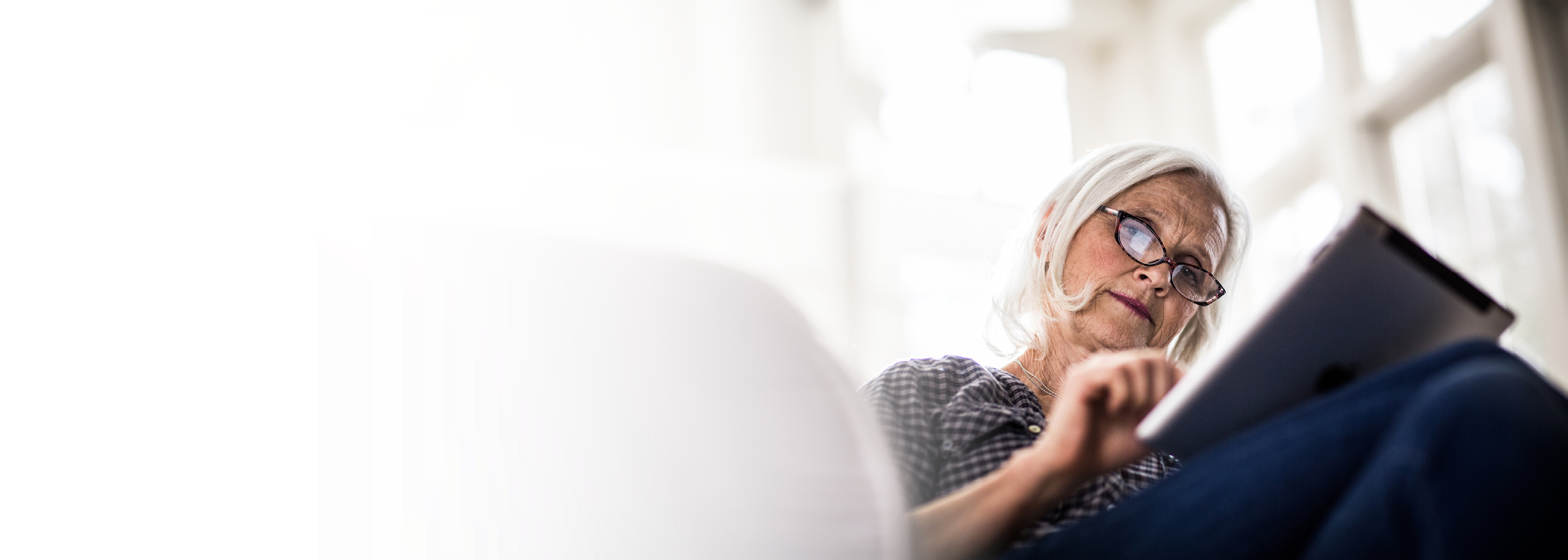 Eine ältere Dame mit Brille arbeitet an ihrem Tablet