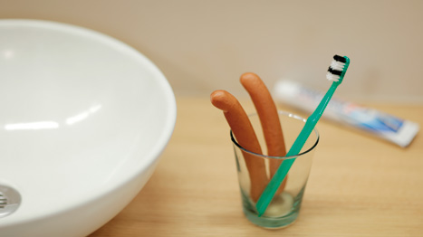 Une paire de saucisses dans un bocal à côté d'une brosse à dents verte.
