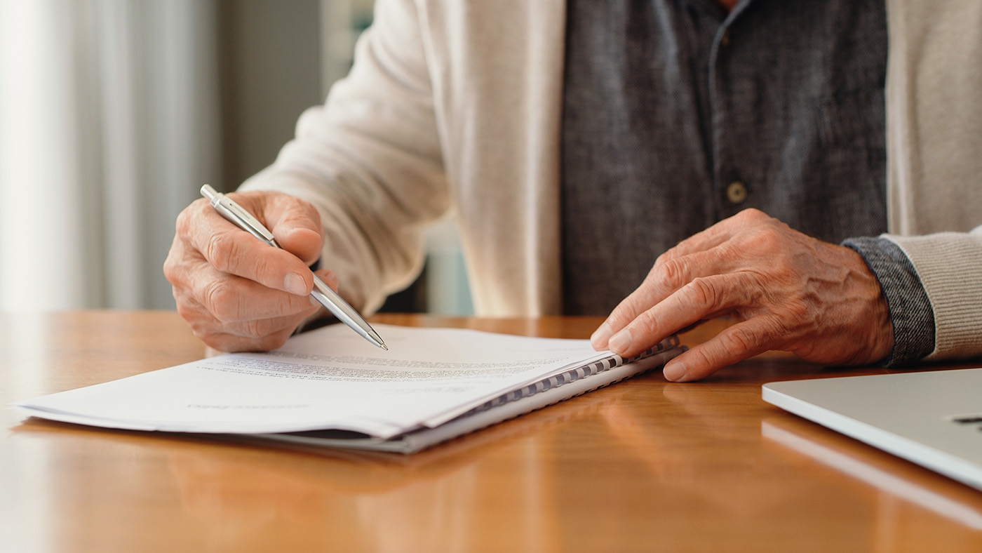 Una persona anziana siede al tavolo con carta e penna.