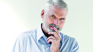 Mann mit grau melierten Haaren hält sich mit der Hand das Kinn und blickt in die Kamera.