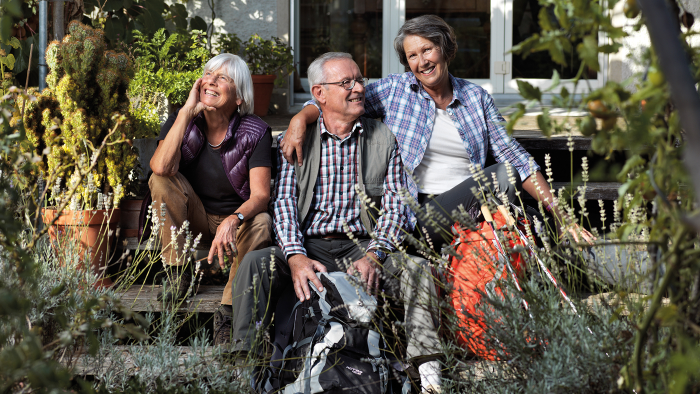 Tre anziani sono seduti in giardino e ridono.
