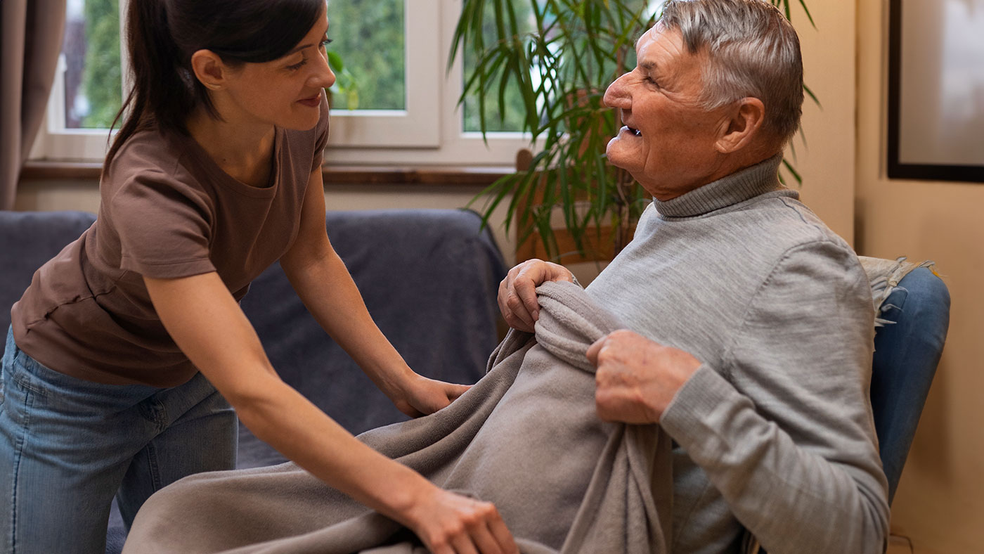 Un assistente mette una coperta sulle ginocchia di un anziano seduto.